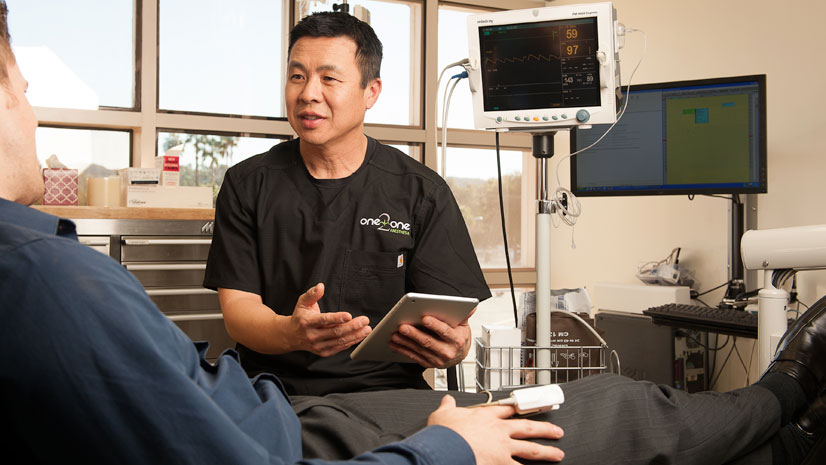 Dr. Ken Lee holding iPad consulting with patient wearing blue shirt in operatory